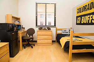 A single residence hall unit with one twin bed, small dresser, desk, and small refrigerator