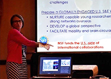 A woman in a red shirt points to a screen showing a PowerPoint presentation